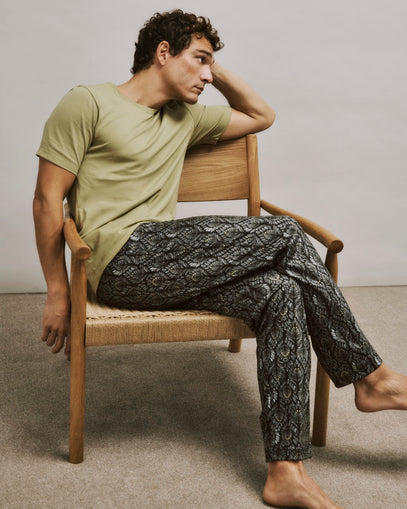 Man sitting on a chair wearing a cardamom shirt and patterned pants.